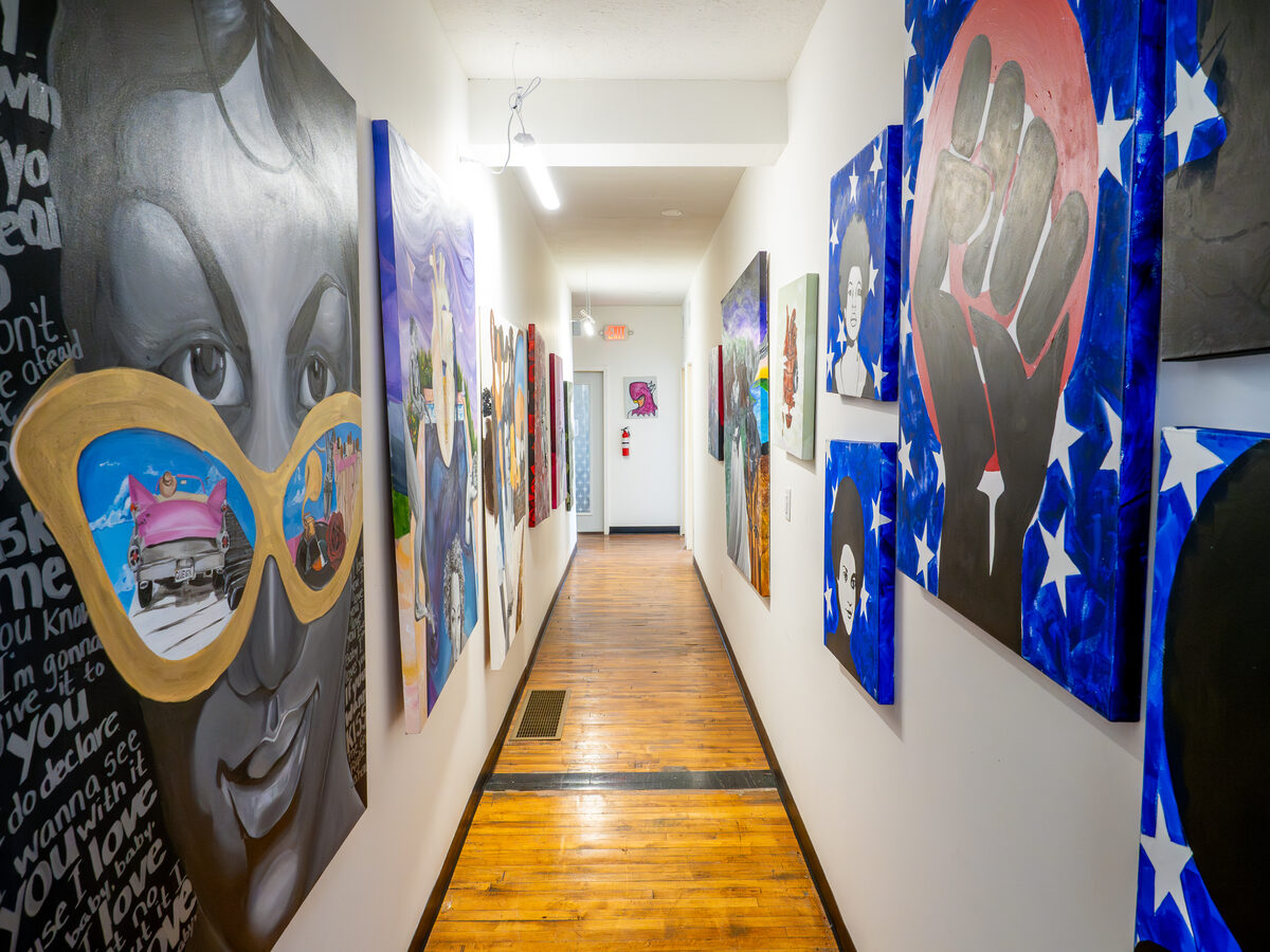 Color in the corridor — a wall of portraits, paintings, and an unmistakable pair of gold sunglasses.