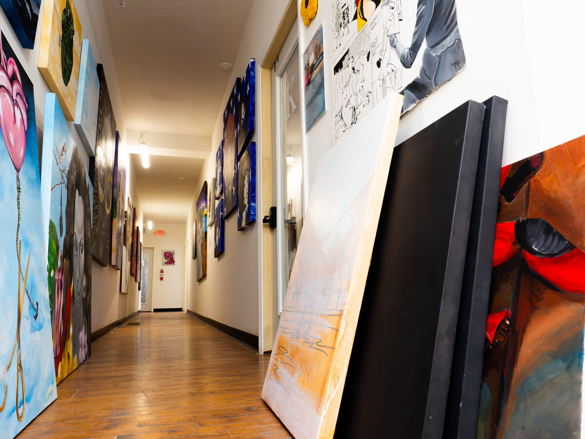 Canvases lean where they last landed. Most days an artist is somewhere down this hall.
