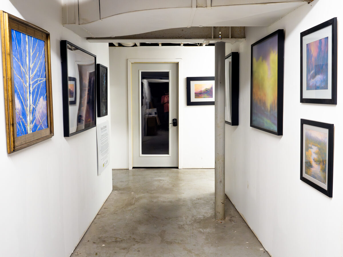 Framed work in the quieter north hallway — landscape painters and printmakers tend to hang here.