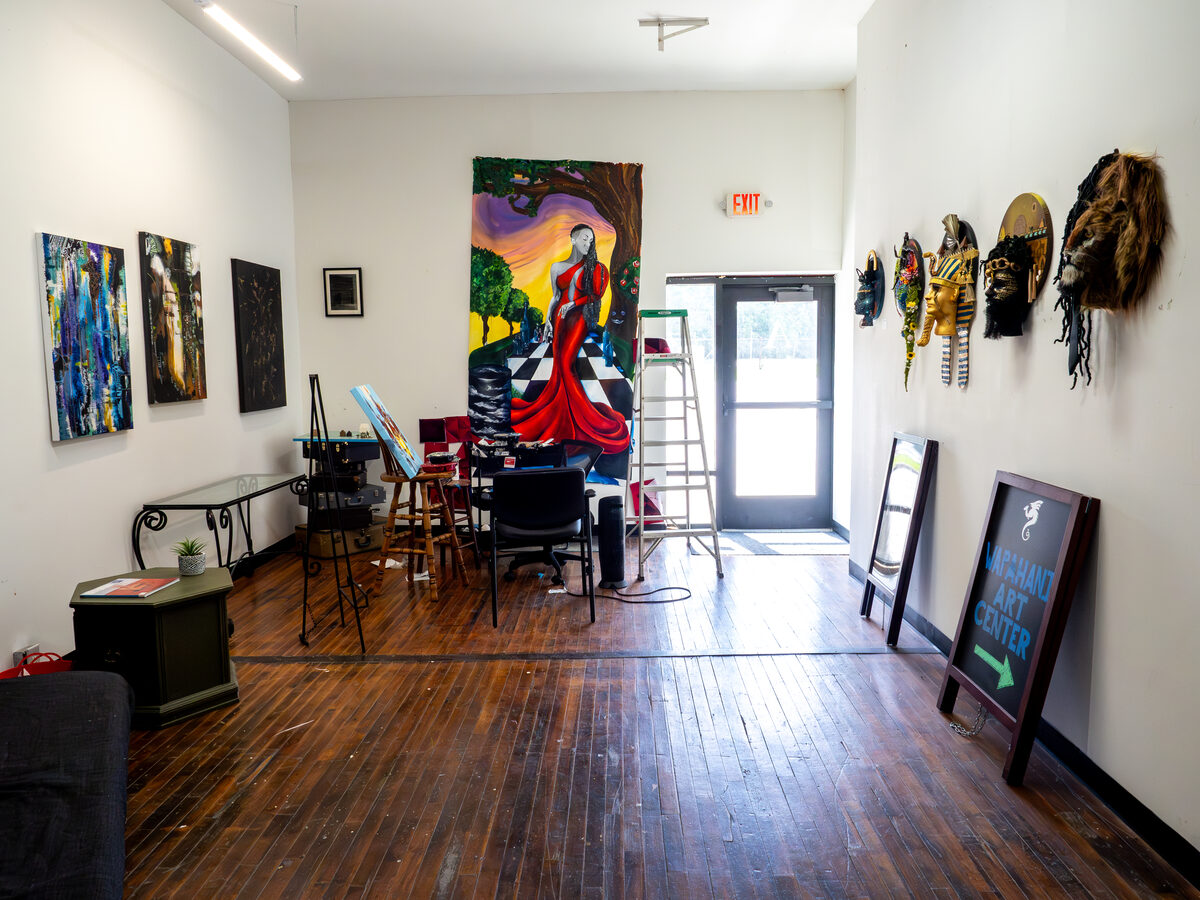 An artist who treats her studio like a small private gallery — paintings, masks, a sandwich-board out front.